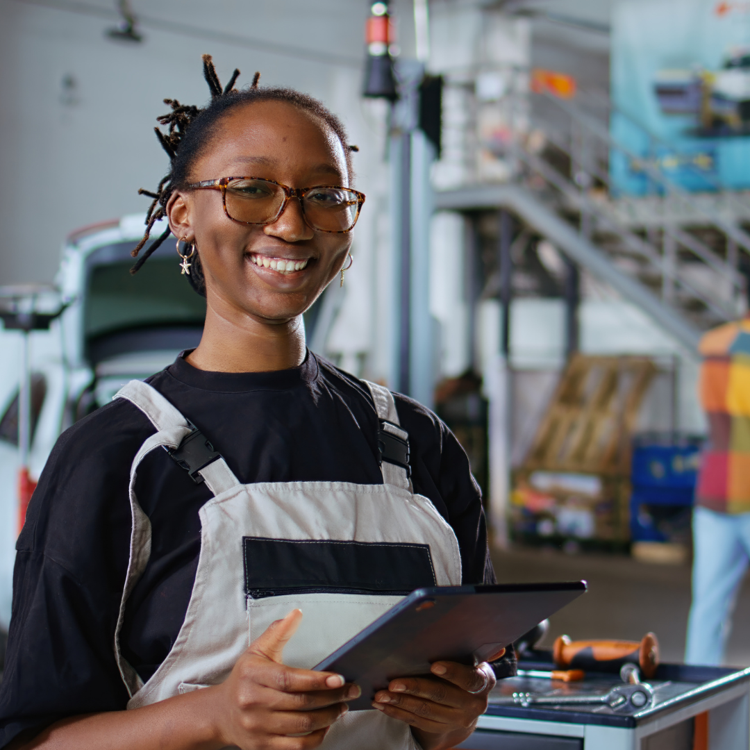 A smiling female engineer in a jumpsuit holding an iPad while looking at the camera
